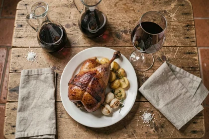Confit de canard servi avec pommes de terre sautées et un verre de vin rouge Bordeaux sur une table en bois rustique