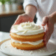 Mains de pâtissier appliquant de la chantilly sur un gâteau lumineux